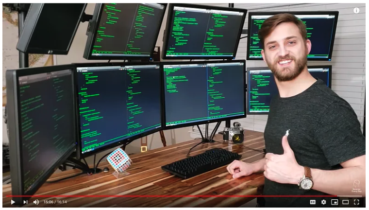 Picture of Carson Davis standing in front of eight monitors.