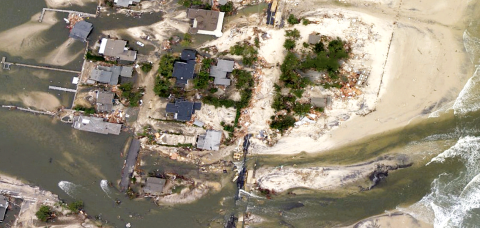 This is an aerial view of coastal flooding in Mantolokig, NJ. This rectangular image shows sandy land, trees, roads, houses, and other structures washed out by flooding water.